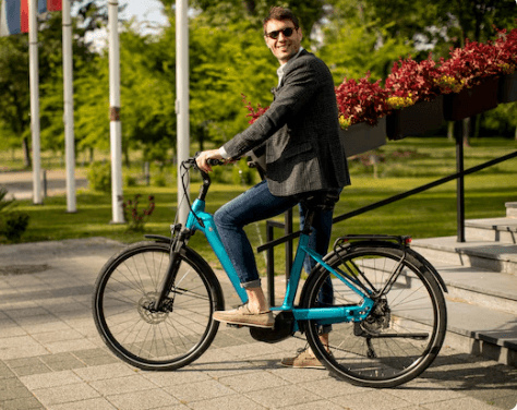 Electric bike in blue, side view, ridden outdoors in a park setting by a person.