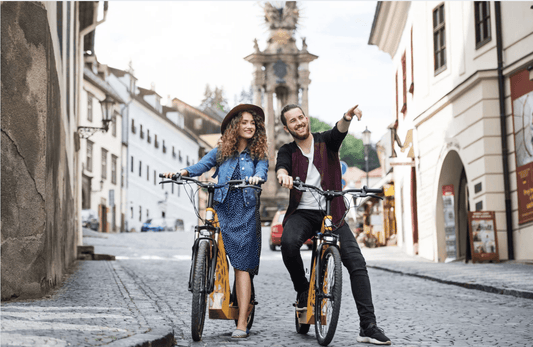 Two people with yellow electric bikes on a cobblestone street in a city setting, front view