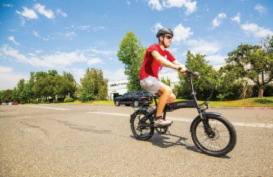 Rider on a black folding electric bike cycling on a sunny city street, side view