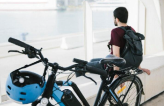 Man with backpack sits by blue electric bike and helmet near water, Pogo Cycles e-bike lifestyle
