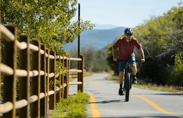 Electric bike being ridden on a scenic paved trail with trees and mountains in the background