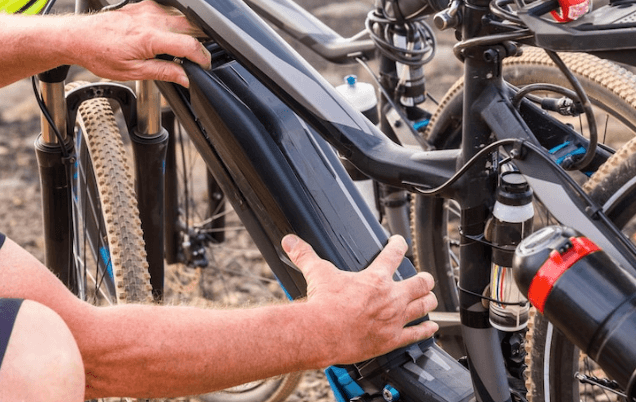 Hands installing a battery on a black electric bike with thick tires outdoors at Pogo Cycles