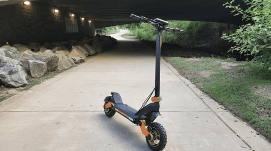 Electric scooter with orange accents on a paved path under a bridge, side view