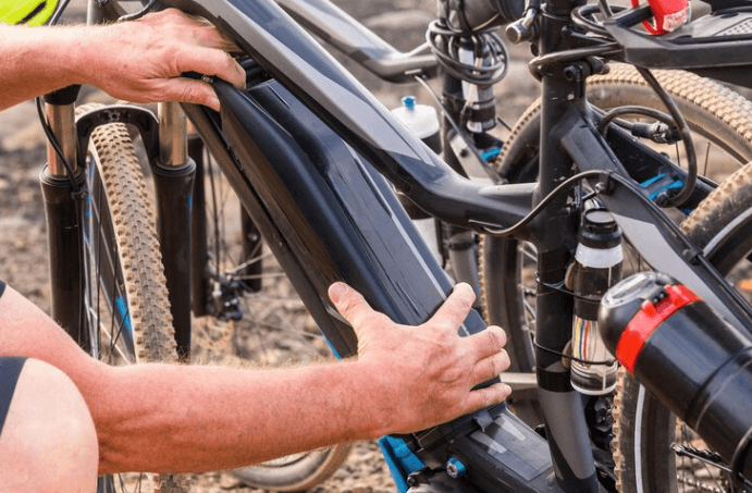 Person installing battery on electric bike frame outdoors, showcasing Pogo Cycles e-bike quality.
